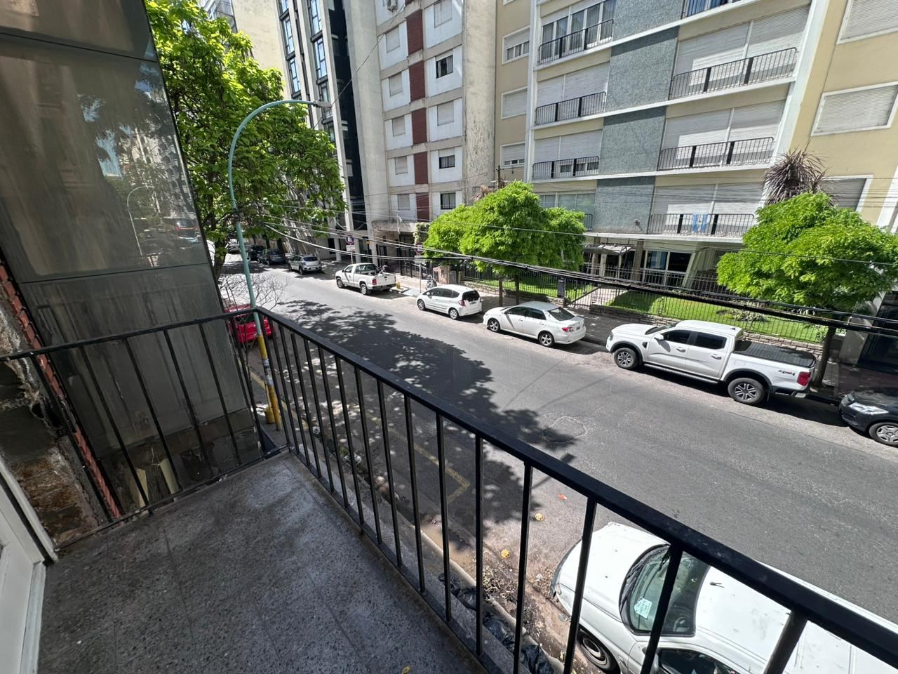 La calle Gascón vista desde el balcón del departamento, con árboles, autos estacionados y edificios de departamentos