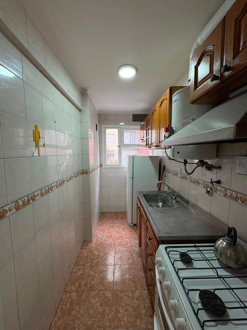 Cocina separada con muebles altos y bajos de madera, mesada con pileta, cocina a gas y ventana al fondo