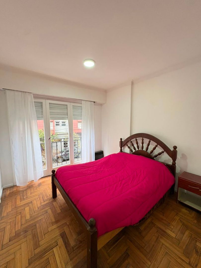 Dormitorio con cama de dos plazas, piso de parquet y puerta ventana a la calle